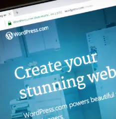 A close-up, angled view of a computer screen displaying the WordPress.com homepage with the large white text "Create your stunning web" on a blue background.