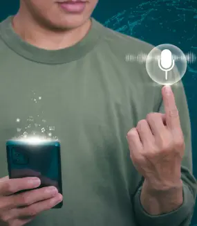A person in a green shirt holds a smartphone, pointing at a glowing microphone icon, indicating voice command use.